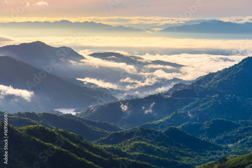 Romantic sea of fog over valley with mountain background at hazy sunrise. Misty evergreen mountain landscape.