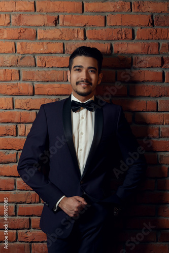 young handsome man in elegant blue suit with butterfly on the brick wall background.