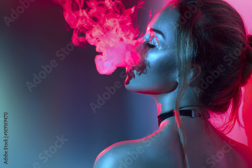 Fashion art portrait of beauty model woman in bright lights with colorful smoke. Smoking girl photo