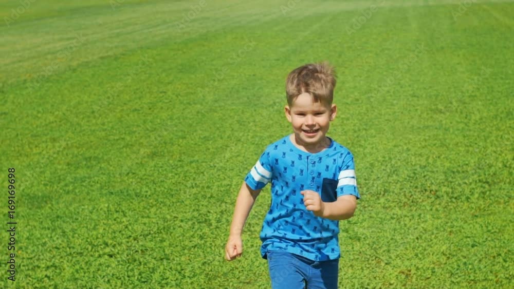 Little boy running across the beautiful green field in summer, very light and happy scene Little boy running across the beautiful green field in summer, very light and happy scene