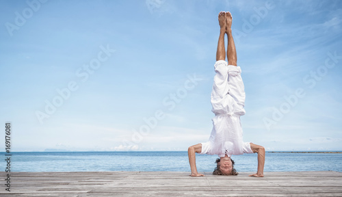 Obraz na plátně Young man doing yoga exercise - headstand, on a beautiful tropical beach