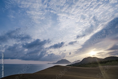 朝日が砂丘に射し込み始める夏の朝の海・島・空の協演