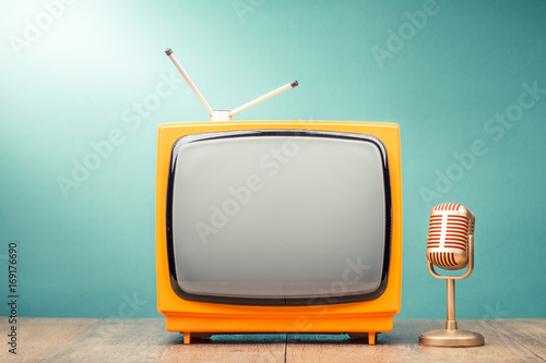 Retro old TV receiver and golden microphone on table front gradient mint green wall background. Broadcasting concept. Vintage style filtered photo