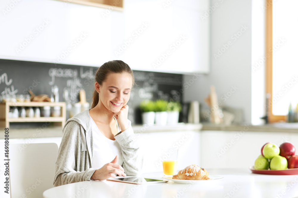 Young woman with orange juice and tablet in kitchen.