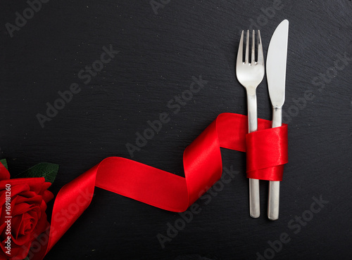 Cutlery and red ribbon on black background