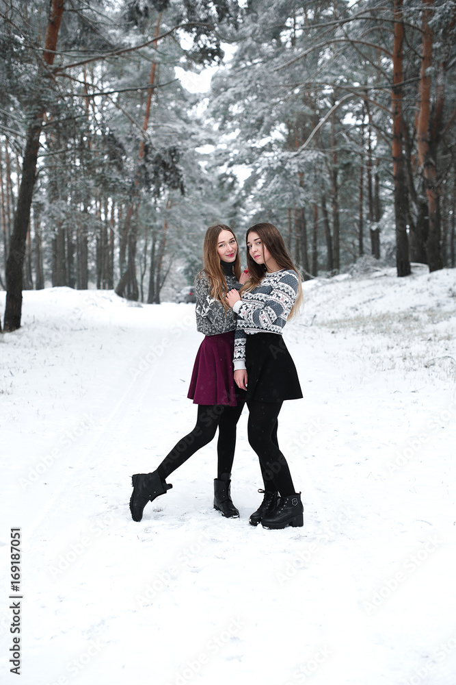 Fototapeta premium Two young teenage hipster girl friends together.Close up fashion portrait of two sisters hugs and having fun winter time,wearing sweater,best friends couple outdoors, snowy weather