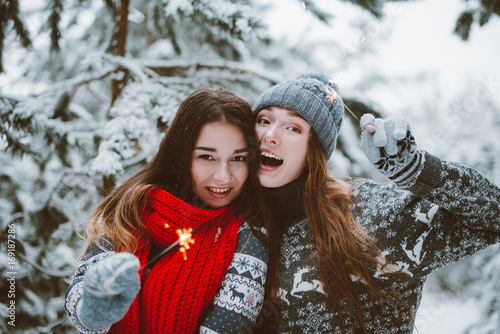 Close up fashion portrait of two sisters hugs and having fun, drinking tea winter time,wearing red santa hats and sweater,best friends couple 