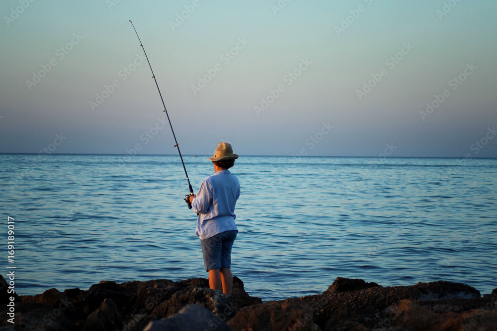 A woman in a hat is fishing with a fishing rod in her hand by the sea coast