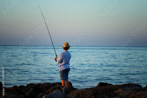 A woman in a hat is fishing with a fishing rod in her hand by the sea coast
