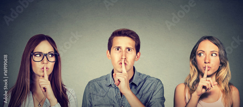 Quadro su tela Secretive young people man and two women with finger to lips gesture