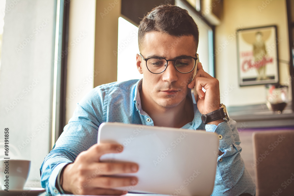 Handsome young businessman is using a tablet and smiling, sitting at bar counter in a modern urban cafe Handsome young businessman is using a tablet and smiling, sitting at bar counter in a modern urban cafe