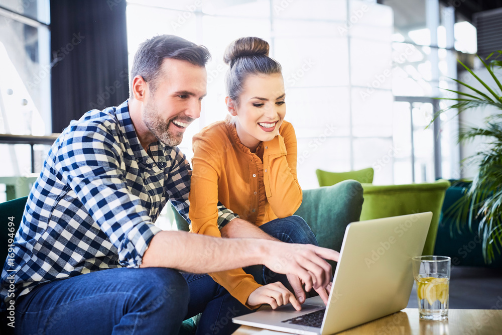 Cheerful couple using laptop browsing and pointing fingers at screen while in modern restaurant Cheerful couple using laptop browsing and pointing fingers at screen while in modern restaurant