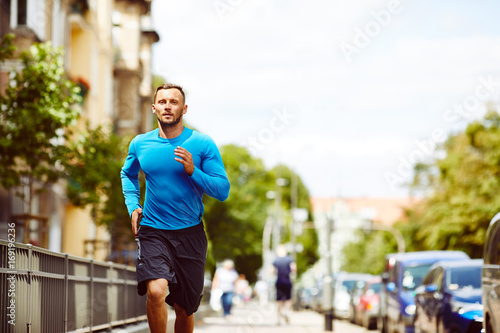 Fototapeta Naklejka Na Ścianę i Meble -  Front view of an athletic man jogging beside a busy city street