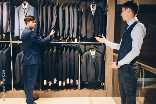 A colleague advises in choosing a suit in a store of luxury clothes for trousers 