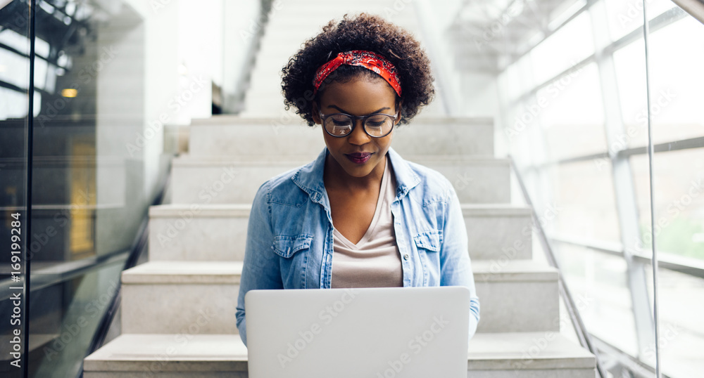 Focused young African student sitting on stairs using a laptop - obrazy, fototapety, plakaty 