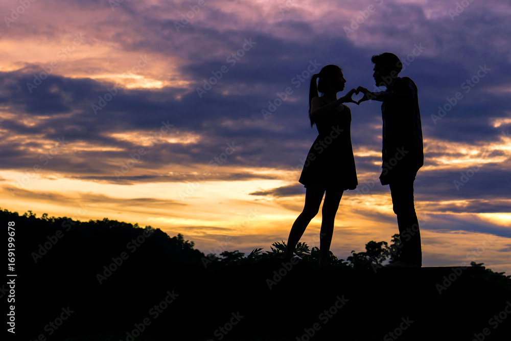 Silhouette couple in love fingers a heart shape as a symbol of love on beautiful sunset background , valentine concept