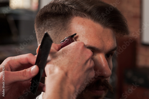 The hands of barber making haircut to young man in barbershop