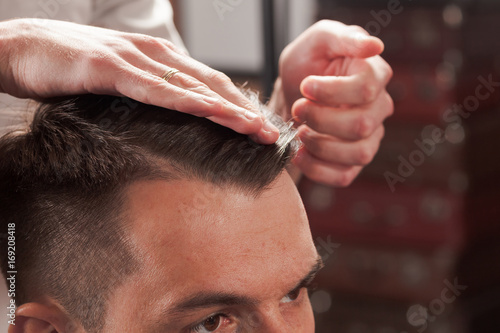 The hands of barber making haircut to young man in barbershop