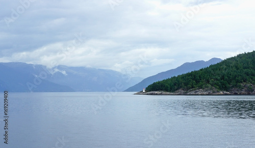 Beacon and silhouette of mountains, view from the ferry, cloudy weather, Norway, Scandinavian landscape with lighthouse