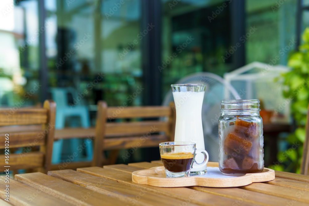 iced cube coffee latte with milk and shot of espresso on the wooden table in the garden.