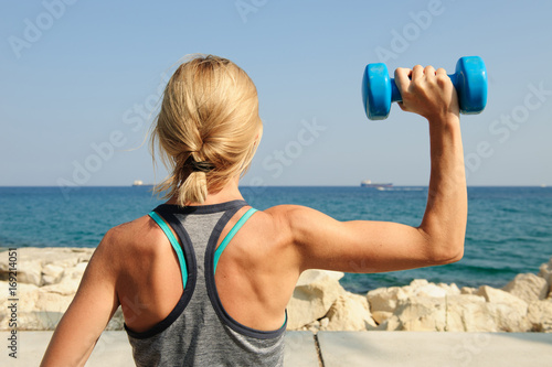 Young athletic woman exercising outdoors: overhead press for upper body strength