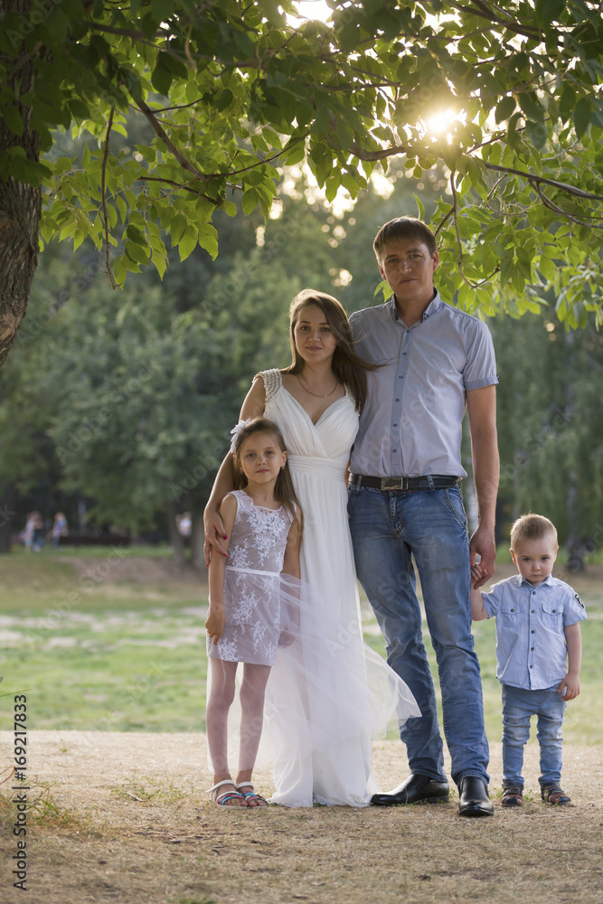 Healthy family posing in the green park - father, mammy, daughter and little boy