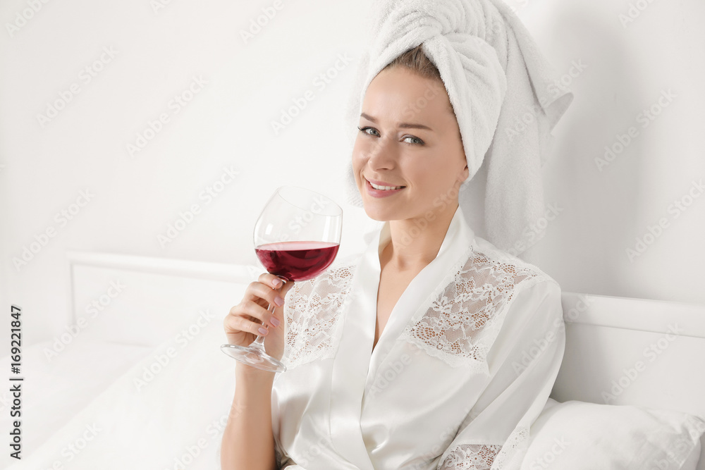 Beautiful young woman in bathrobe after shower with glass of red wine on bed Beautiful young woman in bathrobe after shower with glass of red wine on bed