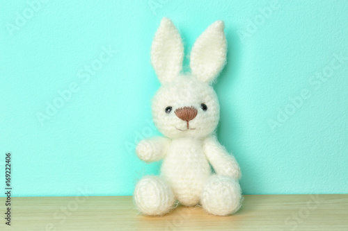 Cute knitted toy bunny on color background