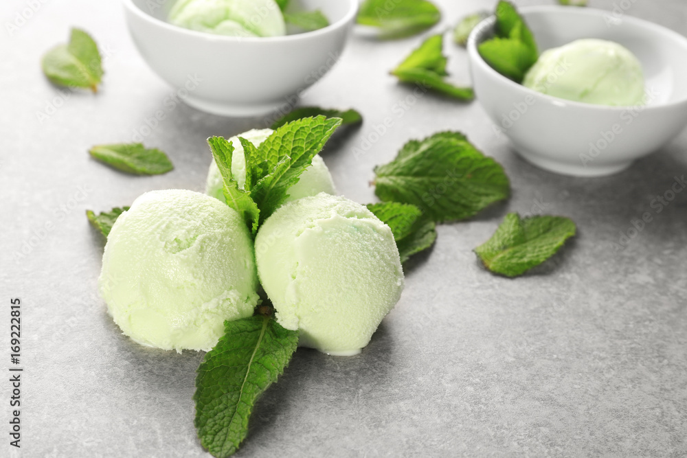 Balls of delicious mint chocolate chip ice cream and fresh leaves on grey table Balls of delicious mint chocolate chip ice cream and fresh leaves on grey table