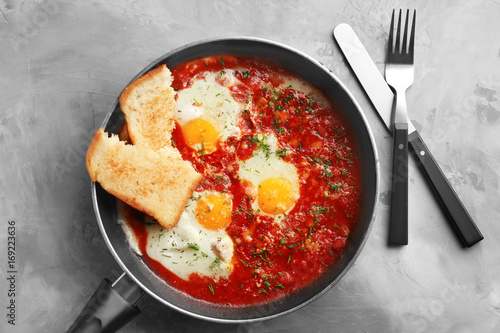 Frying pan with eggs in purgatory on grey background