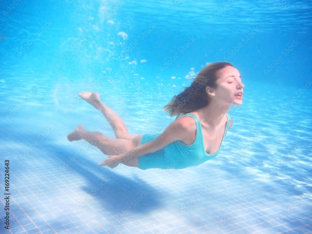 Beautiful young woman swimming under water in pool