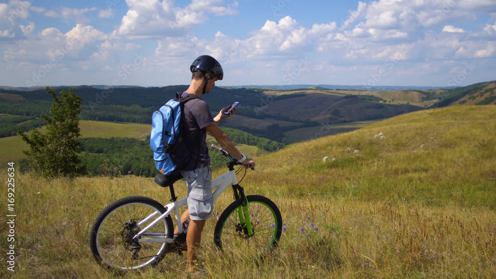 A young man on a bicycle is guided by the terrain using a map on his mobile phone A young man on a bicycle is guided by the terrain using a map on his mobile phone
