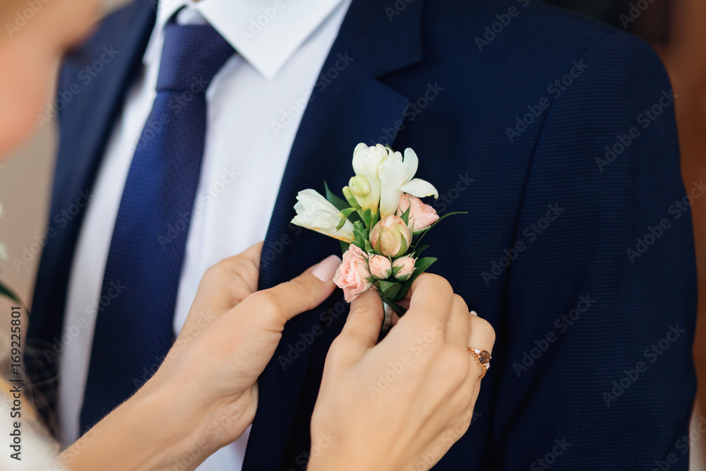 The bride's hand puts on a boutonniere flower on the groom's jac The bride's hand puts on a boutonniere flower on the groom's jac
