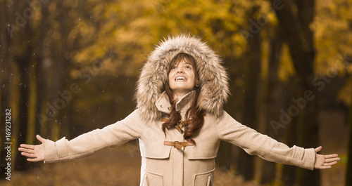 Smiling woman in autumn coat with open arms enjoying the rain