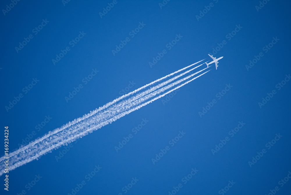 Fototapeta Samolot odrzutowy lecący nad głową po przekątnej szlakiem kondensacji.