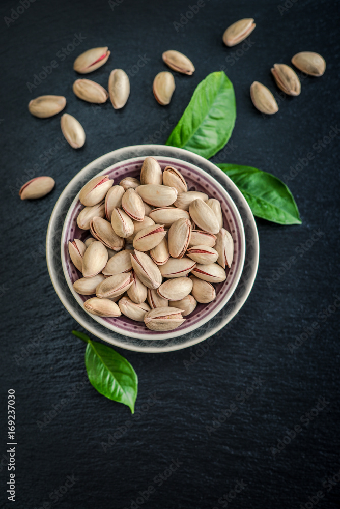 Pistachios in shell on blue plate over black slate background, top view Pistachios in shell on blue plate over black slate background, top view