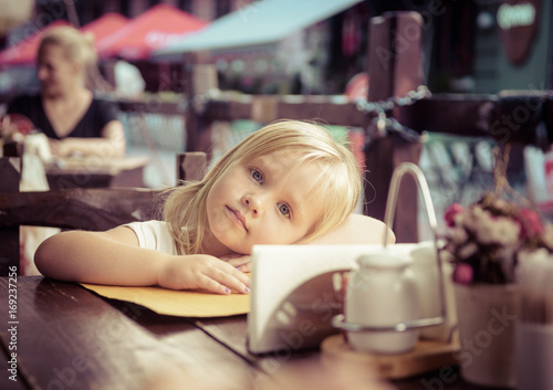little girl sits in street cafe photo