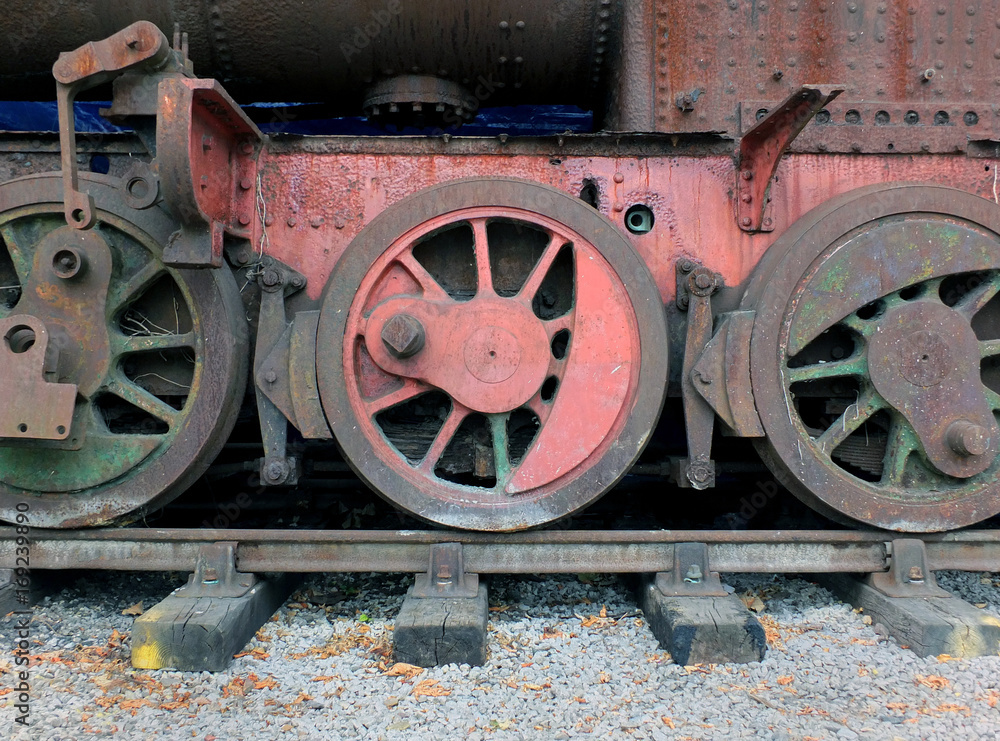 wheels on an old rusting abandoned steam locomotive with red and green faded paint on tracks