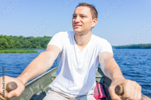 Happy smiling young man rowing boat on lake in Virginia during summer in white shirt