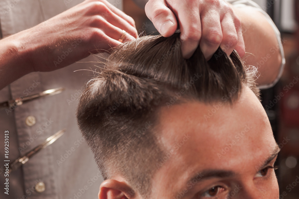 Naklejka premium The hands of barber making haircut to young man in barbershop