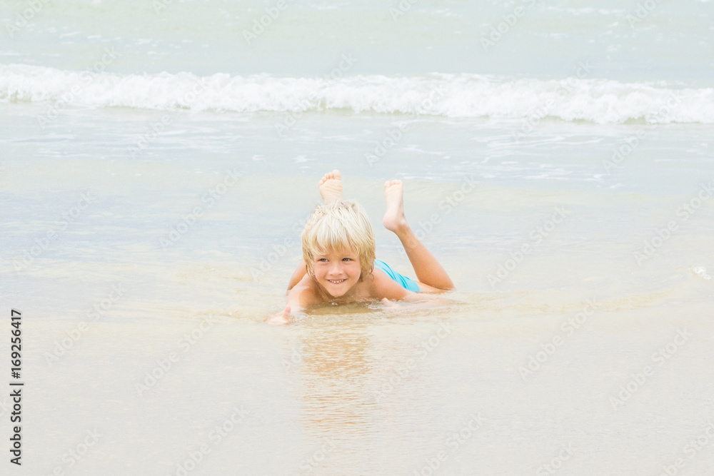 A happy blond boy lies in a water on a beach, Vietnam, Nha-trang