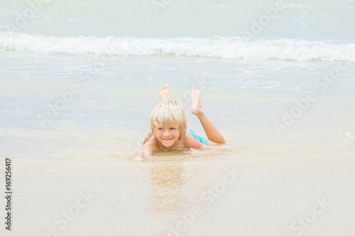 Obraz na płótnie A happy blond boy lies in a water on a beach, Vietnam, Nha-trang w salonie