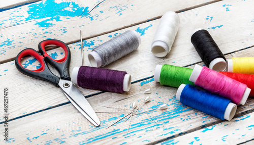 Sewing threads with scissors, needles and pins on the old wooden background.