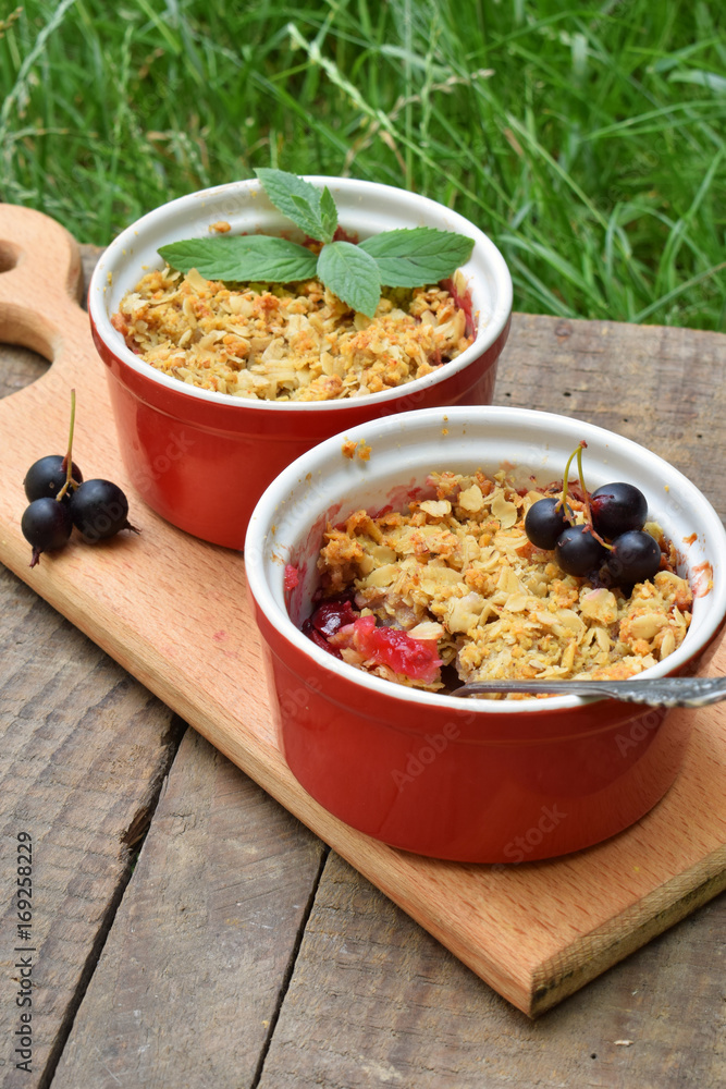 Fruits casserole or crumble with apples and berries in brown cup ramekin on wooden background. Copy space. Photographing with natural light Fruits casserole or crumble with apples and berries in brown cup ramekin on wooden background. Copy space. Photographing with natural light