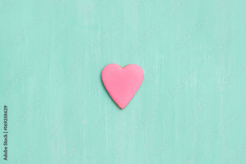 Top view on a pink gingerbread cookie in shape of heart on turquoise background. Flay layout. Love, Valentines's day concept