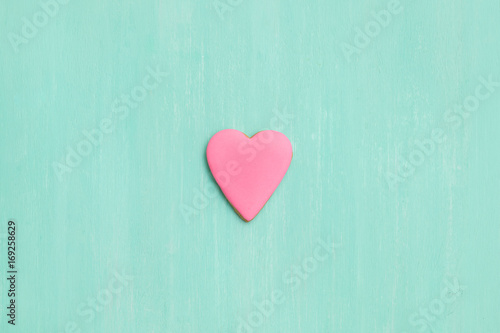 Top view on a pink gingerbread cookie in shape of heart on turquoise background. Flay layout. Love  Valentines s day concept