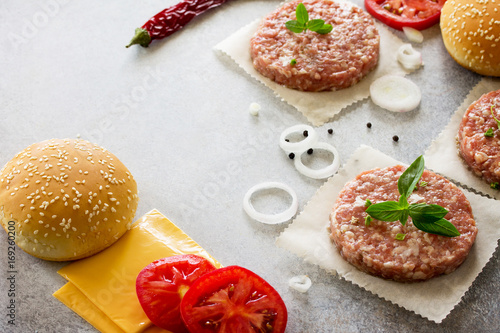Cheeseburger cooking. Ingredients for cheeseburger - raw cutlets, wheat bun, cheese, onion, spices, greens and tomatoes. Fast food. Copy space.