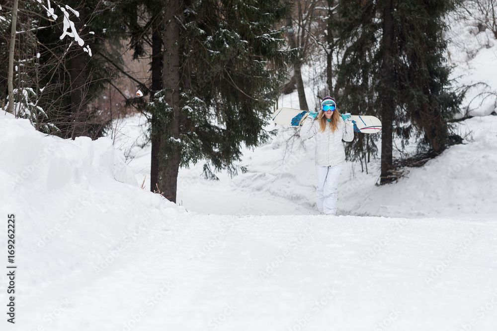 Fototapeta premium Young girl snowboarder goes towards camera on snowy mountain in the forest