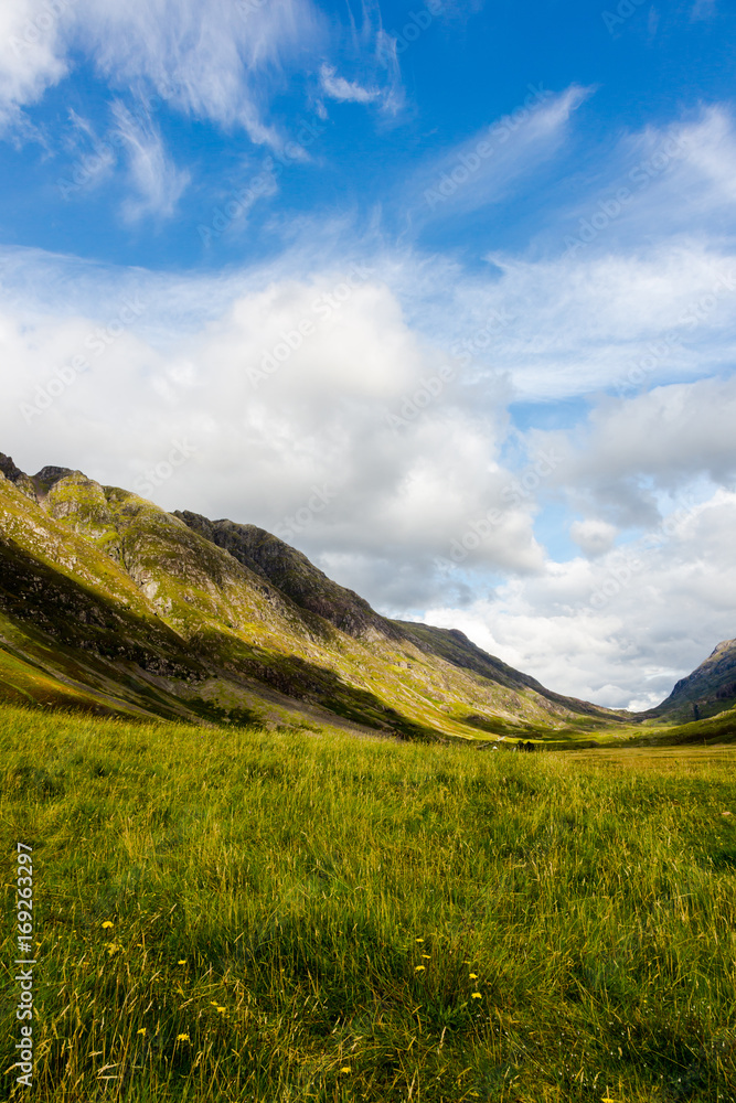 Highlands in Scotland with green meadows, blue sky and white clouds