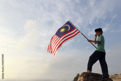 The Concept of Independence Day - a boy holding the Malaysian flag on the shore